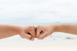 Men hands fist bumping together on blurred sea and sky background. Friendship Day concept.