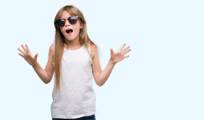 Young blonde toddler wearing sunglasses very happy and excited, winner expression celebrating victory screaming with big smile and raised hands