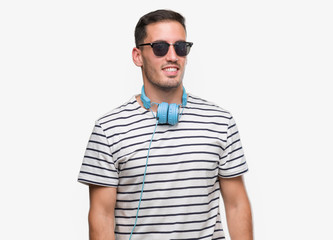 Sticker - Handsome young man wearing headphones looking away to side with smile on face, natural expression. Laughing confident.