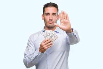 Canvas Print - Handsome young man holding money with open hand doing stop sign with serious and confident expression, defense gesture