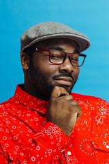 Wall Mural - Thinking man in bright red shirt looking at camera, against bright blue background