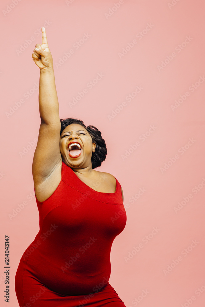 A very happy and excited woman celebrating success with arm up, mouth open and finger pointing up - obrazy, fototapety, plakaty 
