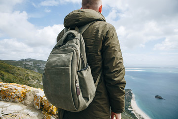 Wall Mural - A tourist or traveler with a backpack is standing on top of a hill and admiring the beautiful view of the ocean or the sea. Walking or hiking