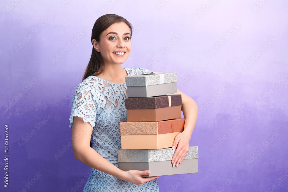 Beautiful young woman with many gift boxes on color background