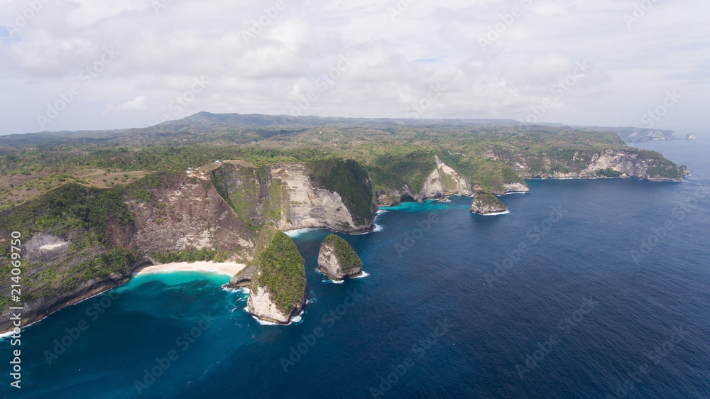 Wild tropical beach at the foot of the cliff. Tropical beach among rocky cliffs. Karang Dawa, Manta Bay or Kelingking Beach on Nusa Penida Island, Bali, Indonesia. Travel concept. - obrazy, fototapety, plakaty 