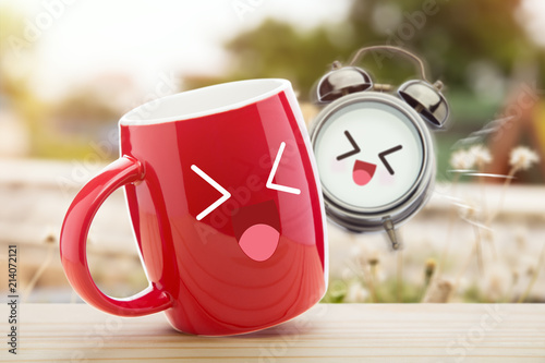 Cuadros en Lienzo Red cup of coffee and alarm clock with a happy smile on wooden table against natural background in the morning