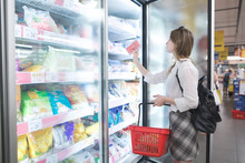 Stylish Woman Buys Frozen Food At A Supermarket. Attractive Young Woman Stands Beside A Freezer And Chooses Frozen Foods. Purchase Of Products In A Supermarket.
