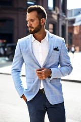 portrait of sexy handsome fashion businessman model dressed in elegant blue suit posing on street ba