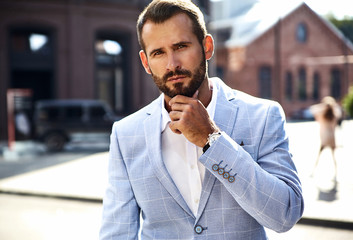 Portrait of sexy handsome fashion businessman model dressed in elegant blue suit posing on street background. Metrosexual