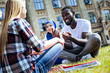 © Viacheslav Yakobchuk - Pleasant conversation. Low angle shot of young people grinning broadly while sitting on grass and chatting together outdoors.