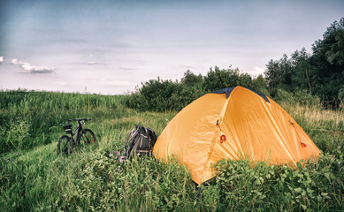 Wall Mural - orange tent with backpack and bicycle on green meadow