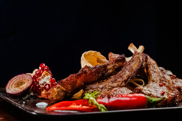 rack of lamb on a black plate decorated with pepper, pomegranate, onion and garlic