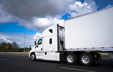 Big rig long haul semi truck transporting goods in semi trailer and running on wide straight highway