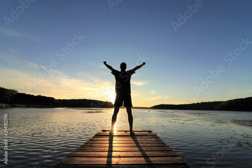 Fotomural Man standing at a landing stage in nature raising his arms to the sky