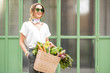 © rh2010 - Portrait of a young woman with bag full of fresh raw vegetables standing outdoors near the green wall