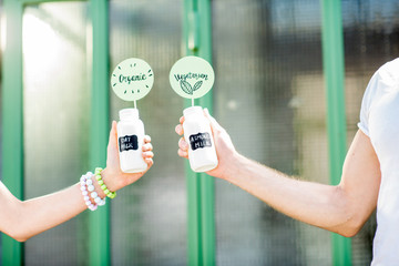 Holding bottles with almond and oat milk with stickers on the green background