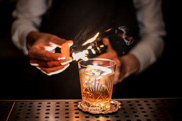 Bartender making a fresh and tasty old fashioned summer cocktail with orange peel and smoke note