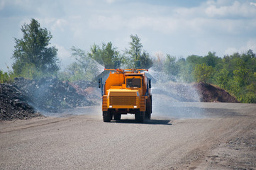 Wall Mural - Heavy truck pours the road with water in the iron ore quarry. Dust removal, protection of the environment. Irrigation of the road from dust