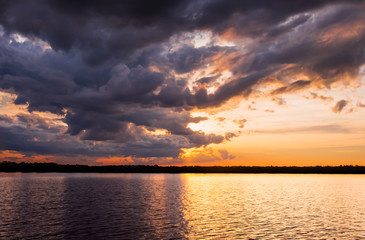 Sunset in the lake. Beautiful sunset behind the storm clouds before a thunder storm above the over lake landscape background. Dramatic sky with cloud at sunset.