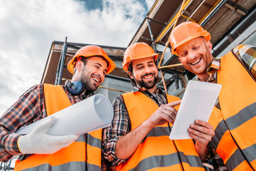 Wall Mural - bottom view of group of builders with blueprint and tablet at construction site