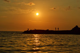 Fototapeta Morze - People's silhouettes at beach on sunset