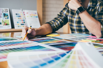 Poster - Young creative Graphic designer using graphics tablet to choosing Color swatch samples chart for selection coloring with work tools and accessories at workplace