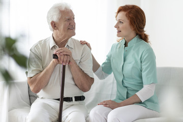 Canvas Print - Friendly caregiver talking with smiling senior man with walking stick