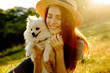 The cute red-haired woman in a hat with a spitz-dog sitting in the park. Beautiful sunset light. Background toning for instagram filter.