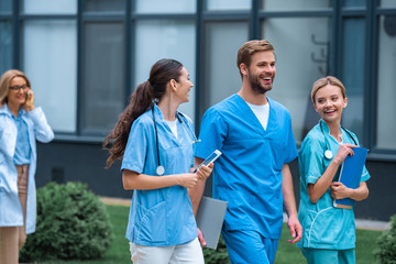 smiling medical students and lecturer walking on street near university