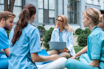 teacher having lesson with students at medical university on green grass