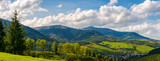 Fototapeta Krajobraz - panorama of mountainous urban area. lovely countryside landscape in early autumn. trees along the road down the hill. village down in the valley and clouds on a blue sky over the distant ridge