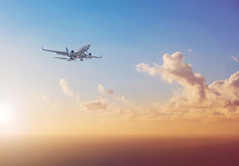 airplane flying above ocean with sunset sky background - travel concept
