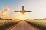 Fototapeta Storczyk - airplane flying above  empty road in rural landscape - travel concept