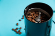 Electric coffee grinder with roasted coffee beans on the kitchen table with blue tabletop. Close-up