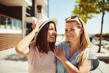 Two laughing young girlfriends walking together in the city