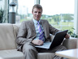 © ASDF - Young businessman sitting at office lobby working with laptop