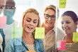 © Flamingo Images - Smiling businesspeople brainstorming with sticky notes on a glas