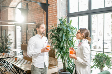 Young couple dressed in white standing together with drinks during the conversation in the beautiful loft interior