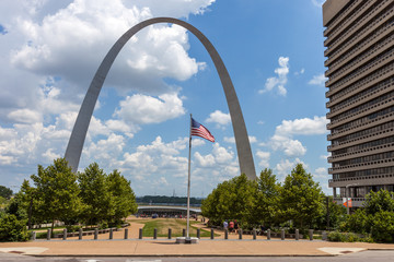 The Gateway Arch in St. Louis, Missouri with the American Flag in front and sky with clouds in the background