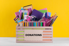 Box With Various School And Office Supplies With A Sign On A Bright Yellow Background. Donation Concept