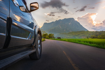 Transportation and car journey concept with SUV car on road and sunset, mountain background.