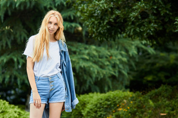 Young girl stands against green trees background