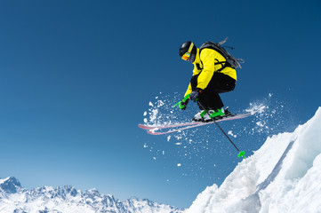 A skier in full sports equipment jumps into the precipice from the top of the glacier against the background of the blue sky and the Caucasian snow-capped mountains. Elbrus region. Russia