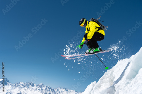 Fotografía A skier in full sports equipment jumps into the precipice from the top of the glacier against the background of the blue sky and the Caucasian snow-capped mountains