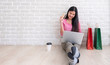 © weedezign - Asian woman in pink casual cloth holding credit card and using laptop to shopping online with bag at white brick wall.Digital technology lifestyle.