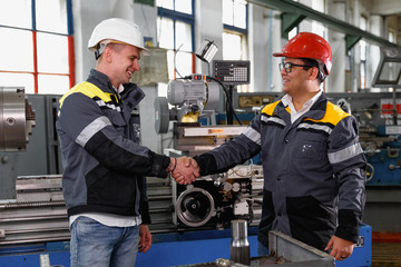 profile shot of two cheerful engineers in protective uniform and hardhats smiling at each other shak