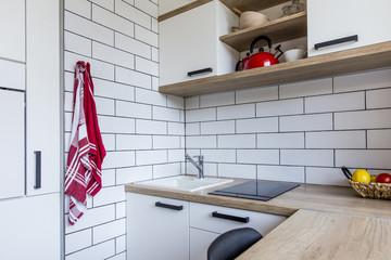 Small tiny white kitchen in panel house in the Czech Republic after the reconstruction with white brick wall and red and oak decoration and oak floor