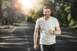 Waist up portrait of happy young man jogging in park in morning. He is training and listening to music with delight. Copy space in left side