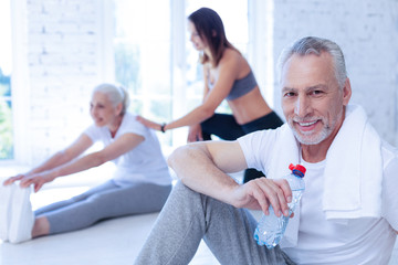 Wall Mural - Help me. Positive delighted male person keeping smile on his face and holding bottle with water in right hand while having rest