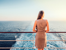 Stylish, Young Woman On An Empty Deck Of A Cruise Ship Against A Background Of Sea Waves, Blue Sky And Sunset